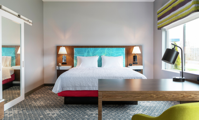 Una amplia suite con cama King, escritorio y silla de un hotel Hampton by Hilton.
